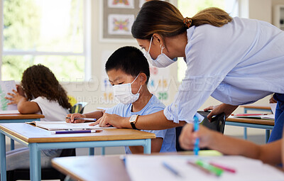 Buy stock photo Education, covid and learning with face mask on boy doing school work in classroom, teacher helping student while writing in class. Elementary child wearing protection to stop the spread of a virus