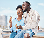 Happy couple at the beach eating an ice cream cone while on a date in nature while on spring vacation. Black man and woman talking and laughing while hugging and having dessert on holiday by seaside.