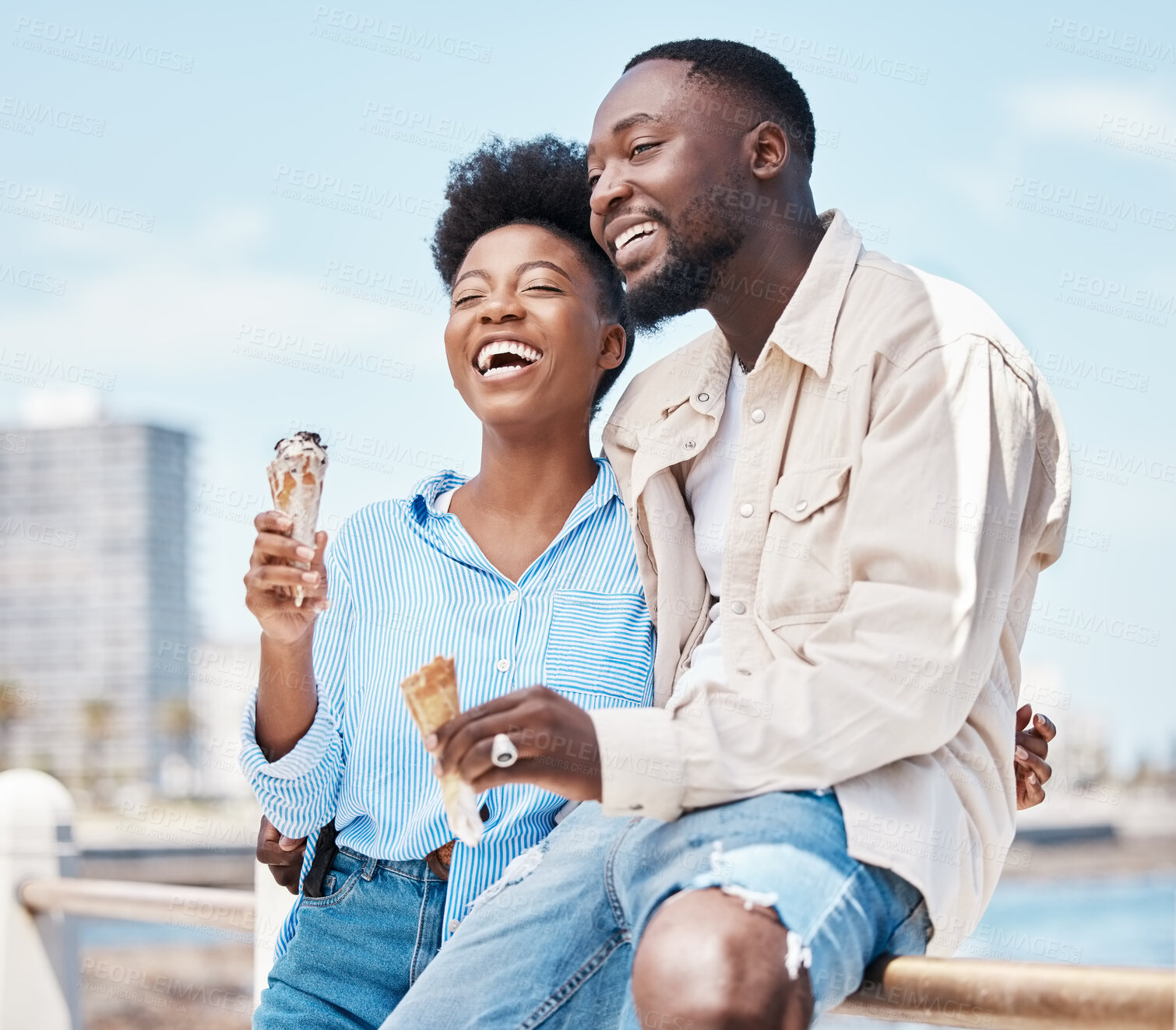 Buy stock photo Happy couple at the beach eating an ice cream cone while on a date in nature while on spring vacation. Black man and woman talking and laughing while hugging and having dessert on holiday by seaside.