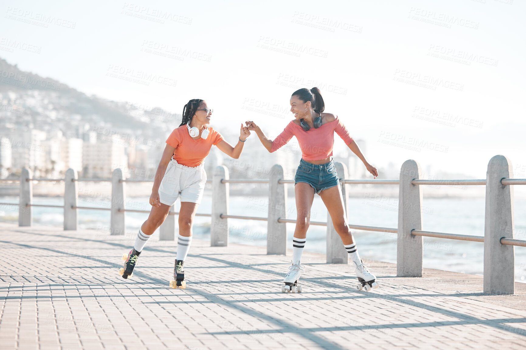Buy stock photo Black women, fist bump and roller skating happy friends by the sea, ocean or shore outdoors. Support, partnership and girl team collaboration or fun while traveling down promenade together.

