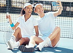 Selfie, sports or couple sitting on a tennis court resting after exercise, practice or training. Wellness, fitness or health with an interracial man and woman with sport racket taking a phone picture