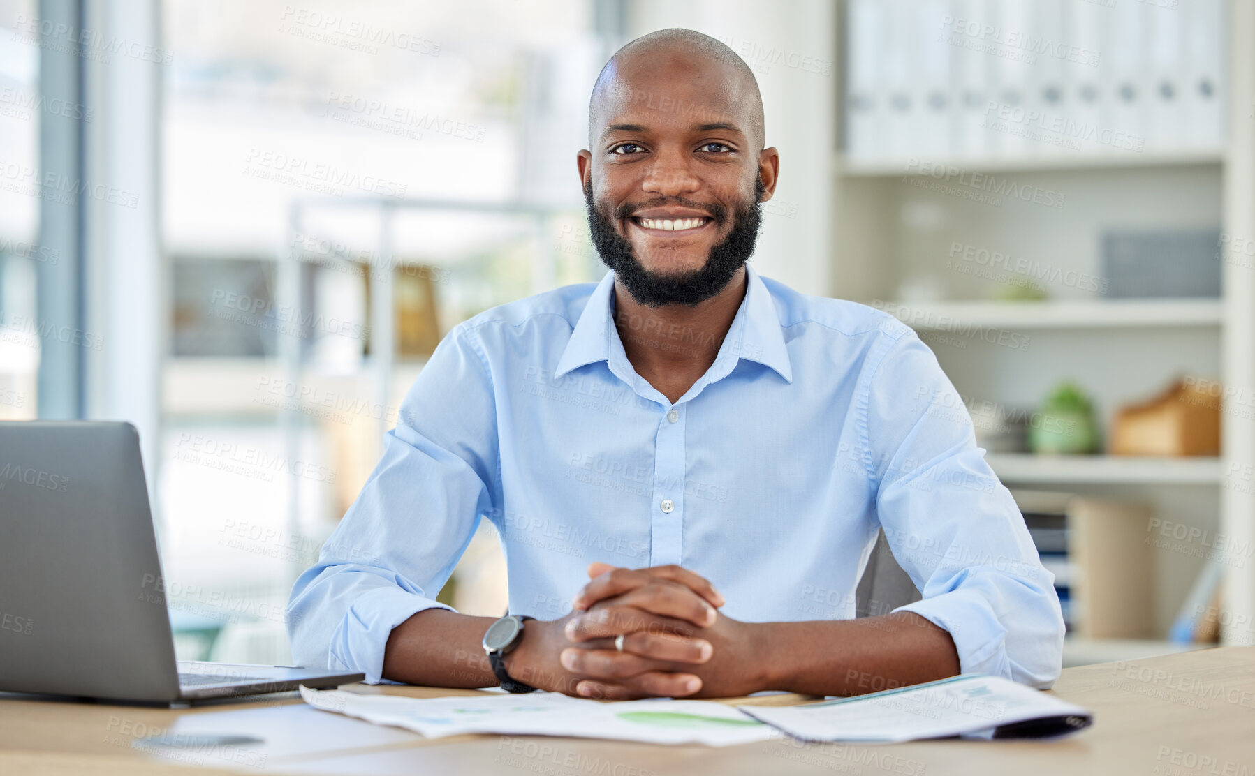 Buy stock photo Portrait of a happy African businessman sitting at his desk in his modern corporate office. Professional black manager working or planning a company project with a laptop and paperwork at a table.