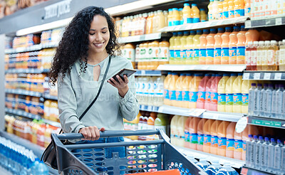Buy stock photo Grocery shopping, phone and woman using technology in a food store with groceries at a shop. Retail customer multitask in a supermarket walking with a mobile in a juice stock aisle and a happy smile