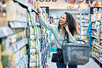 Shopping, phone call and happy woman in a grocery aisle while browsing and choosing products in supermarket, store or shop. Laugh, consumerism and communication while calling and holding food basket