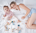 Happy mother, baby on bed and playing with fun educational toys from above. Love, family and early child development, a woman and small girl smiling and spending time together in the bedroom at home.
