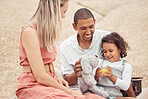 Interracial family, beach travel and summer fun with girl child enjoying bonding time with mother and father during a picnic on rocks. Happy man and woman on vacation or holiday with cute daughter