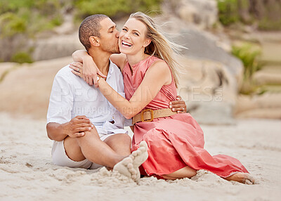 Buy stock photo Beach, multiracial love and a couple kiss in sand while sitting on ocean holiday or honeymoon. A black man and happy woman with smile enjoying nature, weekend and summer vacation at the sea together.