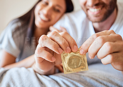 Buy stock photo Condom, couple and sex with the hands of a man opening protection for sexual intercourse in bed with a partner. Happy, love and safe with a woman and her boyfriend using contraceptive in the bedroom