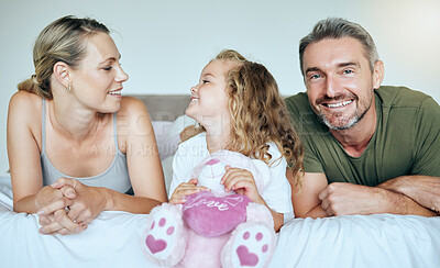 Buy stock photo Happy, smile and family relaxing on a bed while bonding in their calm and comfortable bedroom. Happiness, love and care between parents and a girl child holding a teddy while resting in a modern home