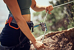 Fitness, safety and hands of rock climbing woman with security, harness cable or sport equipment on mountain cliff outdoor. Travel, hiking and adventure girl with exercise, workout or health training