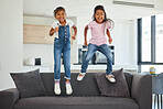 Young friends, jumping and little girls on sofa in fun playful happiness together and excitement at home. Happy energetic kids playing on couch excited in joyful entertainment for free time leisure