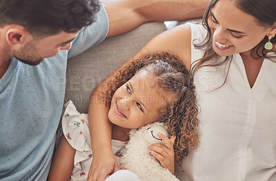 Buy stock photo Love, family and girl bonding on a sofa with her parents, loving and caring in a living room at home. Happy, relax and smiling mother and father embracing their daughter, enjoy moment of parenthood