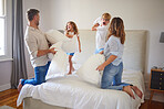 Family pillow fight, in parents bedroom and kids smile with happiness. Children jump on bed, playing with mom and dad at home. Happy bonding time, having crazy fun and laughing on a weekend together 