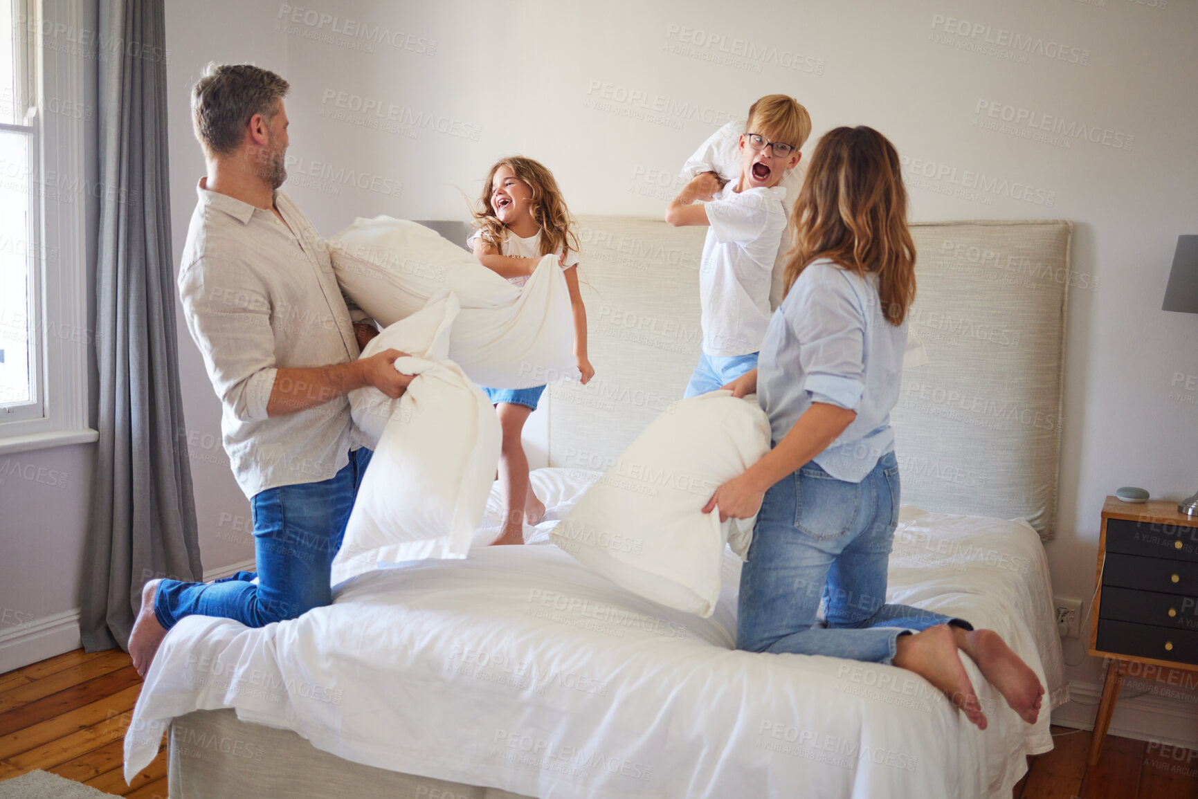 Buy stock photo Family pillow fight, in parents bedroom and kids smile with happiness. Children jump on a bed, playing with mom and dad at home. Happy bonding time, having crazy fun and laughing together with energy