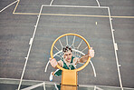 Portrait of basketball player hanging on hoop on a basketball court. Young man playing basketball outside doing slam dunk and jumping to score a point. Motivation to win and have fun in sports game