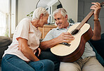 Senior man and woman with guitar on the sofa at home, enjoying retirement. Old couple playing music on instrument, having fun and laughing together. Elderly husband plays love tune or song for wife