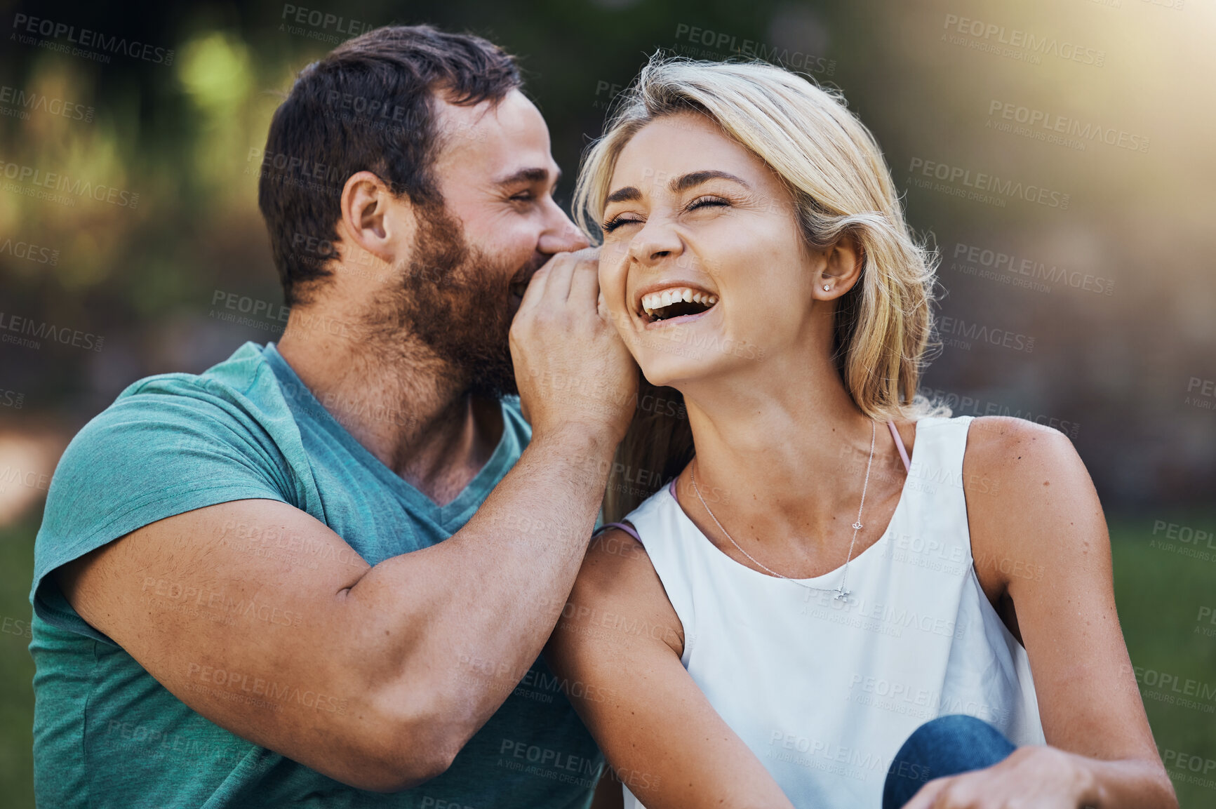 Buy stock photo Gossip, secret and funny story with couple on a romantic date in nature in Australia in summer. Man talking in a whisper into the ear of a young laughing woman while happy in a garden together