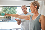 Fitness, health and senior couple doing exercise in the living room of their comfortable home. Happy, smile and healthy elderly woman doing arm workout with motivation from her husband in retirement.