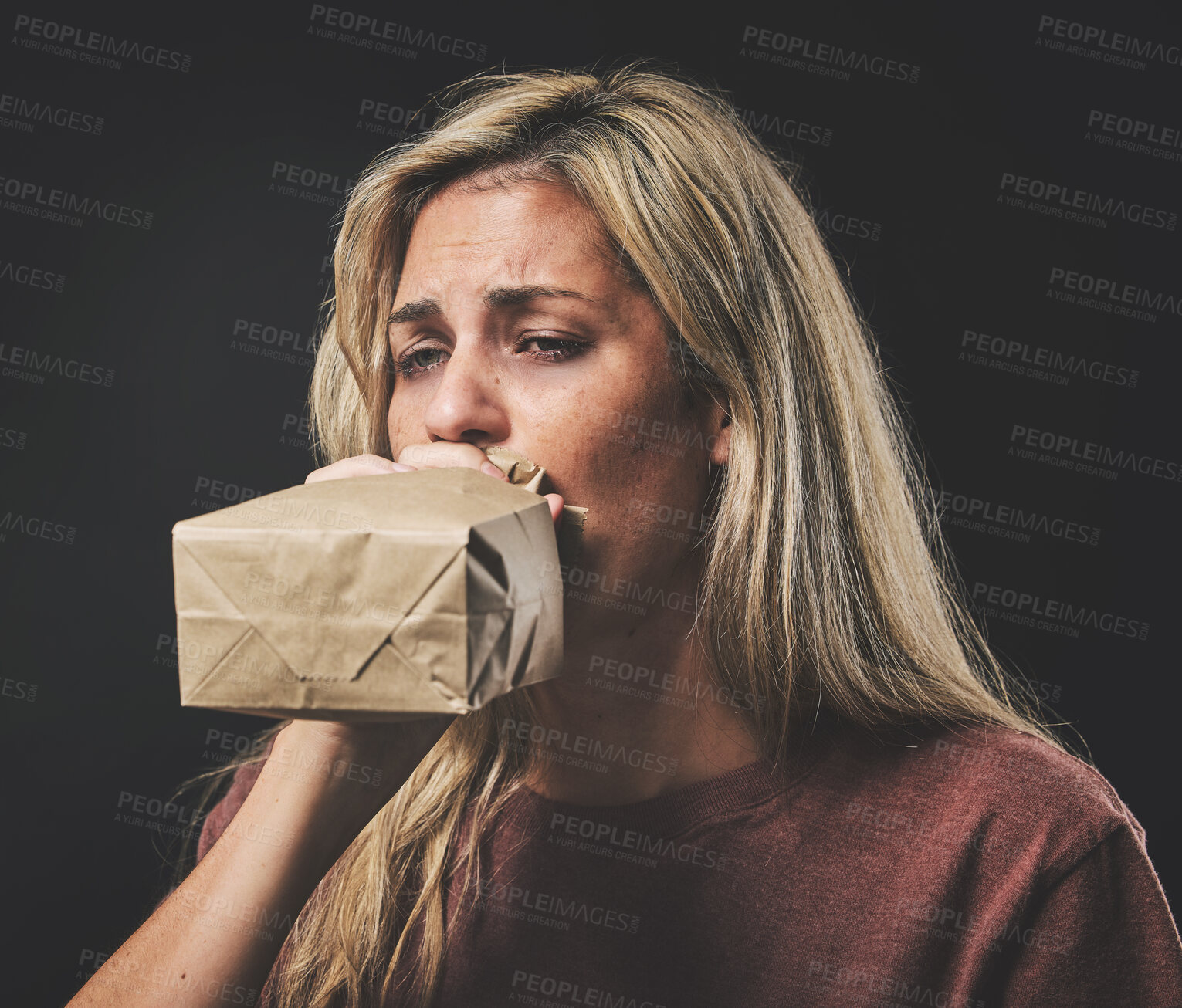 Buy stock photo Anxiety, scared woman breathing into paper bag on dark background for mental health or psychology mockup. Young girl experience fear, panic or asthma attack breathe air for stress, sad and depression