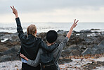 Girl friends with arms raised on beach looking at sea two young women celebrating travel freedom