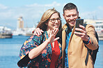 Happy couple taking photo using smartphone in harbour watefront sharing vacation photographing holiday memories with mobile phone camera