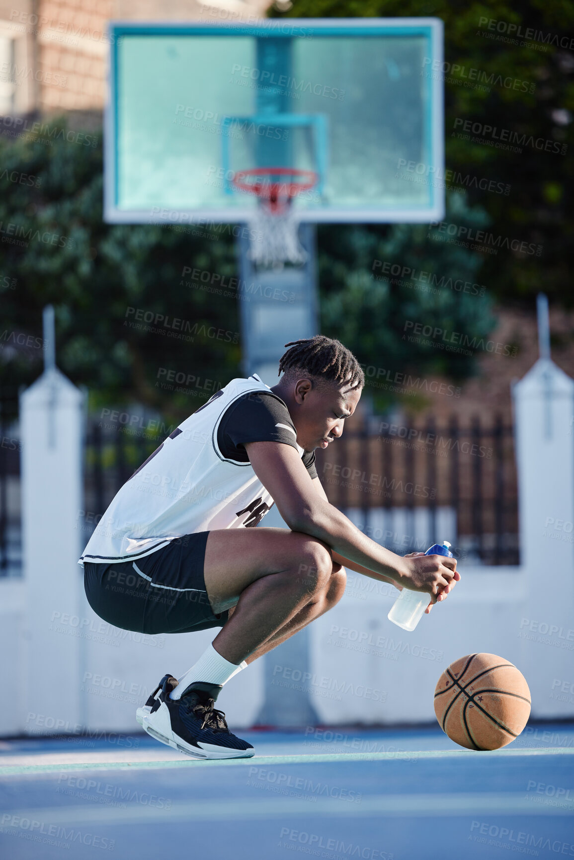Buy stock photo Basketball, sport and fitness with a young man on a court for exercise, training and workout. Health, wellness and fitness with a sporty person resting and drinking water after sports practice