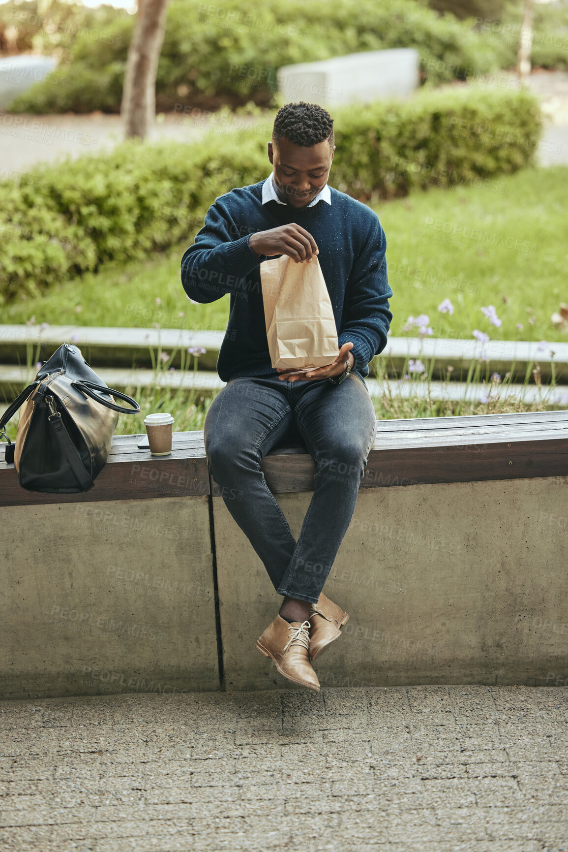 Buy stock photo Black business man on a lunch break in the city, sitting and eating a meal or sandwich in a brown paper bag. Hungry worker relaxing with a tasty snack, food on the go for a professional entrepreneur