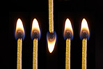 Fire and flame burning on matches sticks as light in the dark against black studio background. Closeup detail of a row of five bright art or artistic matchsticks with flames lit for heat
