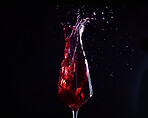 Wine, alcohol or drink glass and splash on black studio background for celebration, cheers or restaurant toast. Zoom, red creative texture or fruit beverage in liquid motion at event or birthday