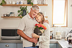 Flower bouquet, hug and senior couple with smile for celebration of marriage in kitchen of their house. Elderly man and woman giving roses as gift while hugging for love, anniversary or birthday