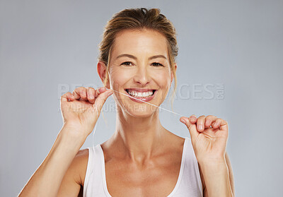 Buy stock photo Dental, healthcare and oral hygiene with a woman flossing her teeth and taking care of her mouth in studio on a gray background. Health, hygiene and floss with a mature female looking after her smile