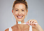 Senior woman and portrait with toothbrush for dental wellness and teeth whitening in grey studio. Mature, healthy and happy lady with toothpaste for mouth cleaning and white smile face mockup.

