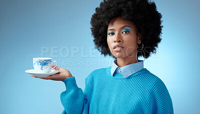 Buy stock photo Tea, fashion and blue with a black woman in makeup on a wall background in studio holding a cup and saucer. Face, portrait and afro with a young female posing for drink, beverage and refreshment