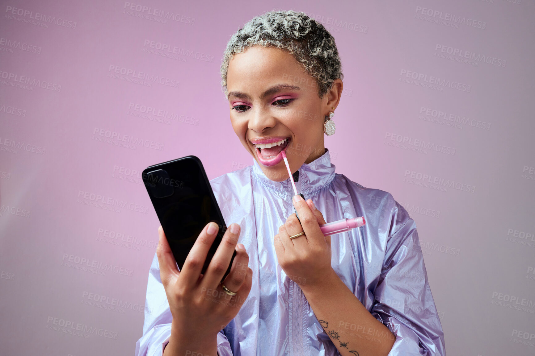 Buy stock photo Fashion, phone and woman using lipstick in studio for beauty, makeup and mouth cosmetics routine alone. Social media influencer applying pink lip gloss for selfcare against a grey studio background