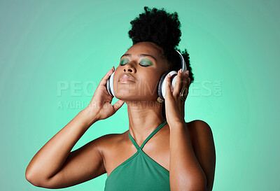 Buy stock photo Black woman in green studio with headphones on, listening to music. Young happy girl with makeup, cosmetics and beauty with wireless earphones streaming a song, podcast or radio for fun and to relax