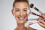 Makeup, beauty and woman with foundation brushes in studio portrait with facial cosmetics and skincare products. Smile, and happy make up artist or beautician and elegant face model with mockup space