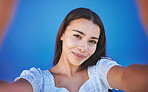 Smile, happy and taking selfie with woman showing face during travel against blue background. Pov portrait of smiling female with natural beauty taking a photo and having fun for social media