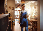 Woman, happy and apron in restaurant working as waitress with food menu in hand for table. Girl, smile and service work at luxury diner, cafe or coffee shop show happiness on face for job in London