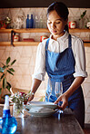 Waitress, restaurant and clean at table for plate, glass and cutlery in apron with sanitizer. Woman, cafe or coffee shop cleaning with apron, bottle and spray after customer put dishes in Cape Town