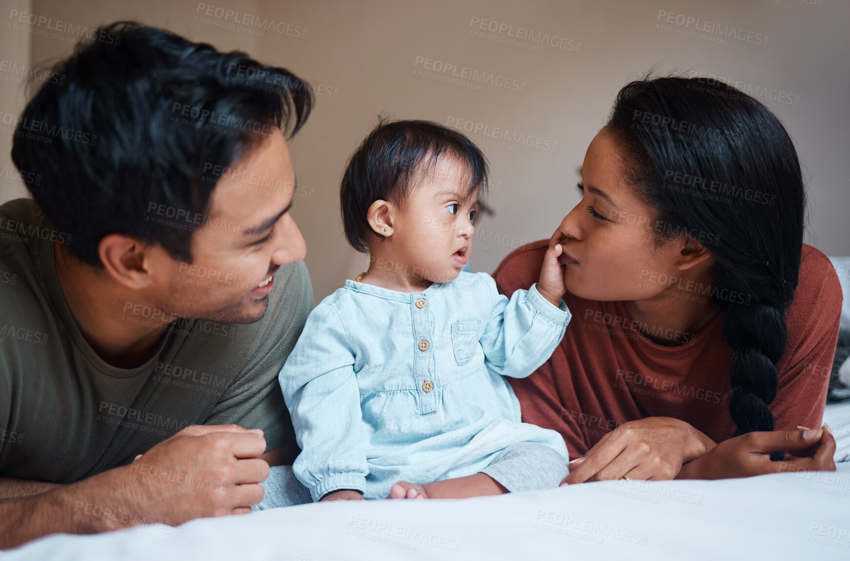 Buy stock photo Family, parents and Down syndrome baby with love, care for relaxing and spending quality time together at home. Mother and father relax on bed playing with new born child with genetic disorder