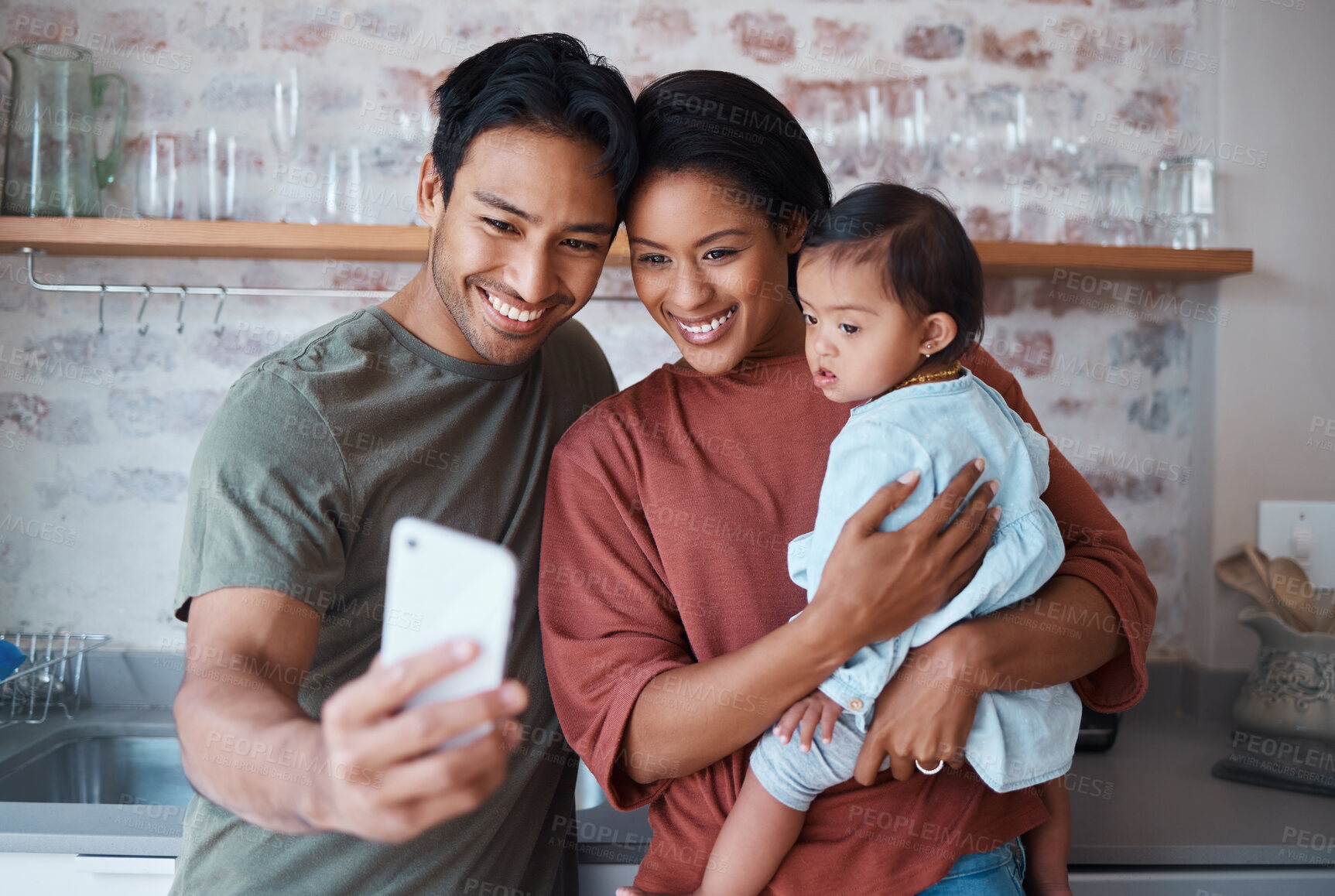 Buy stock photo Happy, parents and baby with down syndrome taking selfie together in kitchen of family home. Happiness, smile and mother and father bonding with disabled child while taking picture on phone in house.