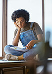 Young woman, reading book and relaxing on a window sill looking calm, focus and peaceful at home. Smart female student studying literature or educational book in her free time in her cozy apartment
