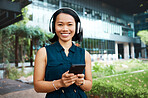 Asian woman, headphones and phone while streaming music, videos or podcast standing outside on break feeling free and happy on internet. Portrait and smile of happy business female using technology 
