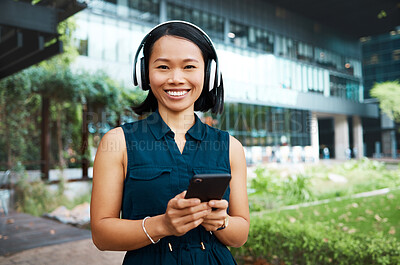 Buy stock photo Asian woman, headphones and phone while streaming music, videos or podcast standing outside on break feeling free and happy on internet. Portrait and smile of happy business female using technology 