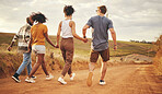Support, holding hands and friends on a vacation in the countryside walking on a dirt road. Nature, freedom and happy group of people in the desert on a summer holiday, journey or adventure.
