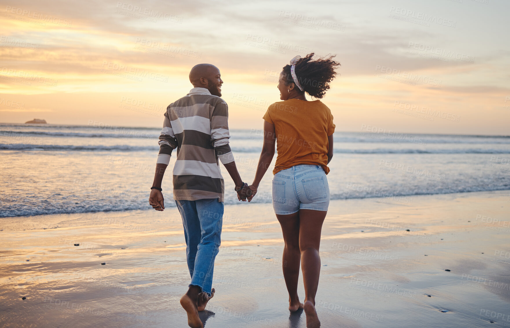 Buy stock photo Black couple, holding hands and on beach with sunset for romance, celebrate relationship or holiday together. Love, happy man and woman bare feet, relax or smile on romantic seaside vacation or break