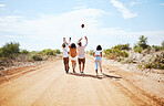 Summer, adventure and friends walking on dirt road in the country, throwing ball in air. Travel, freedom and young group of men and women on holiday together to explore nature, vacation and blue sky
