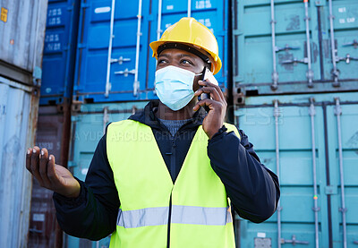 Buy stock photo Covid, logistics and black man on phone call while working at a container warehouse. African industrial manager talking about shipping, delivery and cargo on a mobile with a face mask at storage site