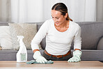 Living room, cleaner and woman cleaning table with product, spray bottle and rubber gloves in modern home. Happy worker in apartment using soap liquid, hygiene detergent for spring clean service
