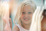 Fashion, girl and happy shopping child at shopping mall store, boutique or retail shop for discount sales clothes on rack. Happiness, smile and young kid or youth customer looking at fabric product
